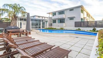 Zona junto a la piscina con sillones, una piscina y un edificio moderno con balcones.