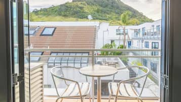 A balcony with a table and two chairs, overlooking a hillside and buildings.