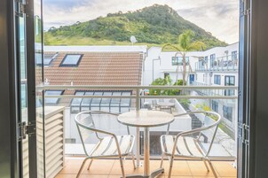 Un balcón con una mesa y dos sillas, con vistas a una colina y edificios.