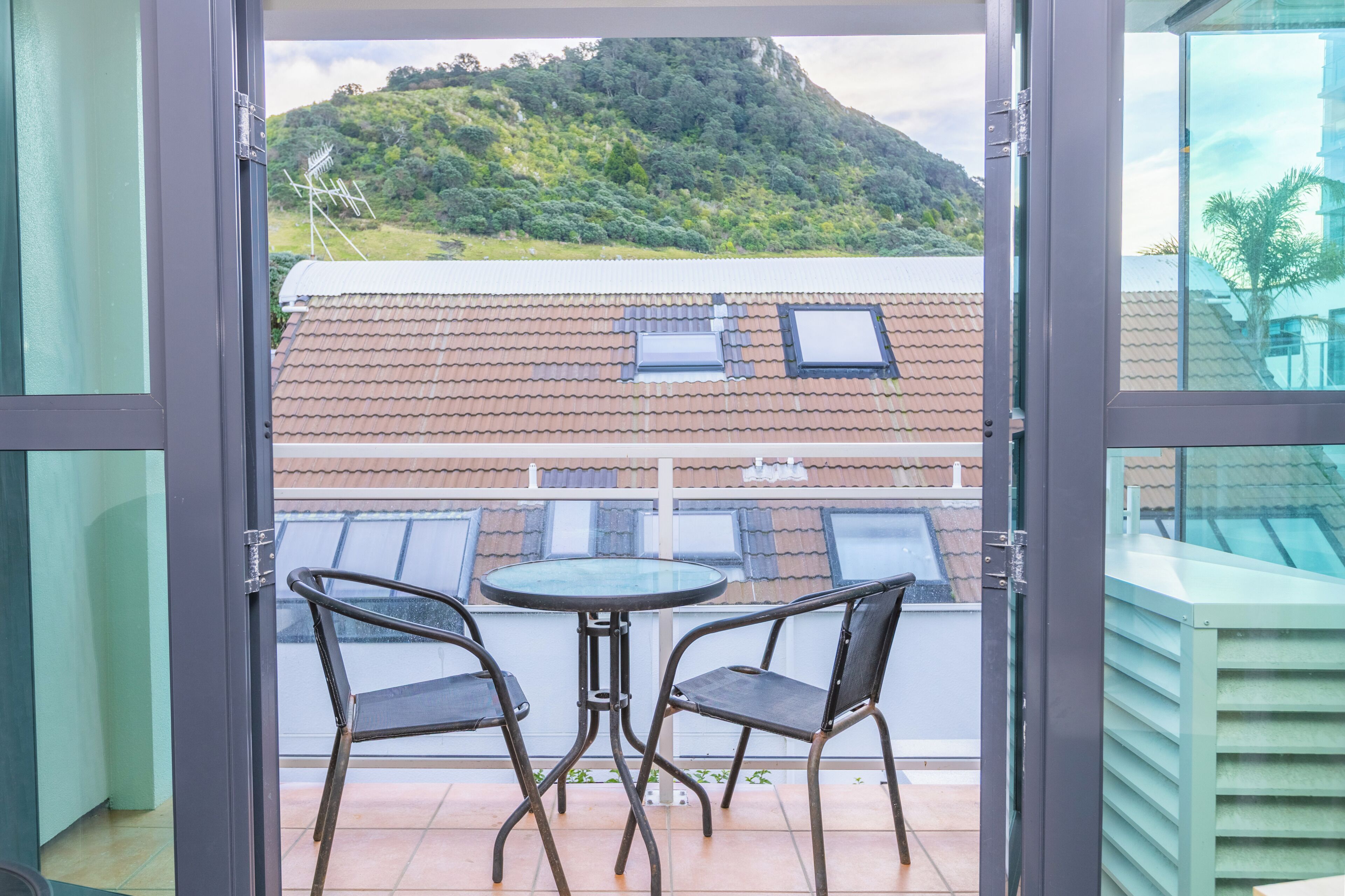 A balcony with two chairs and a table, overlooking a hillside with buildings.