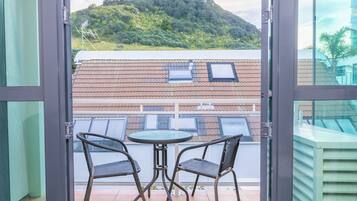 A balcony with two chairs and a table, overlooking a hillside with buildings.