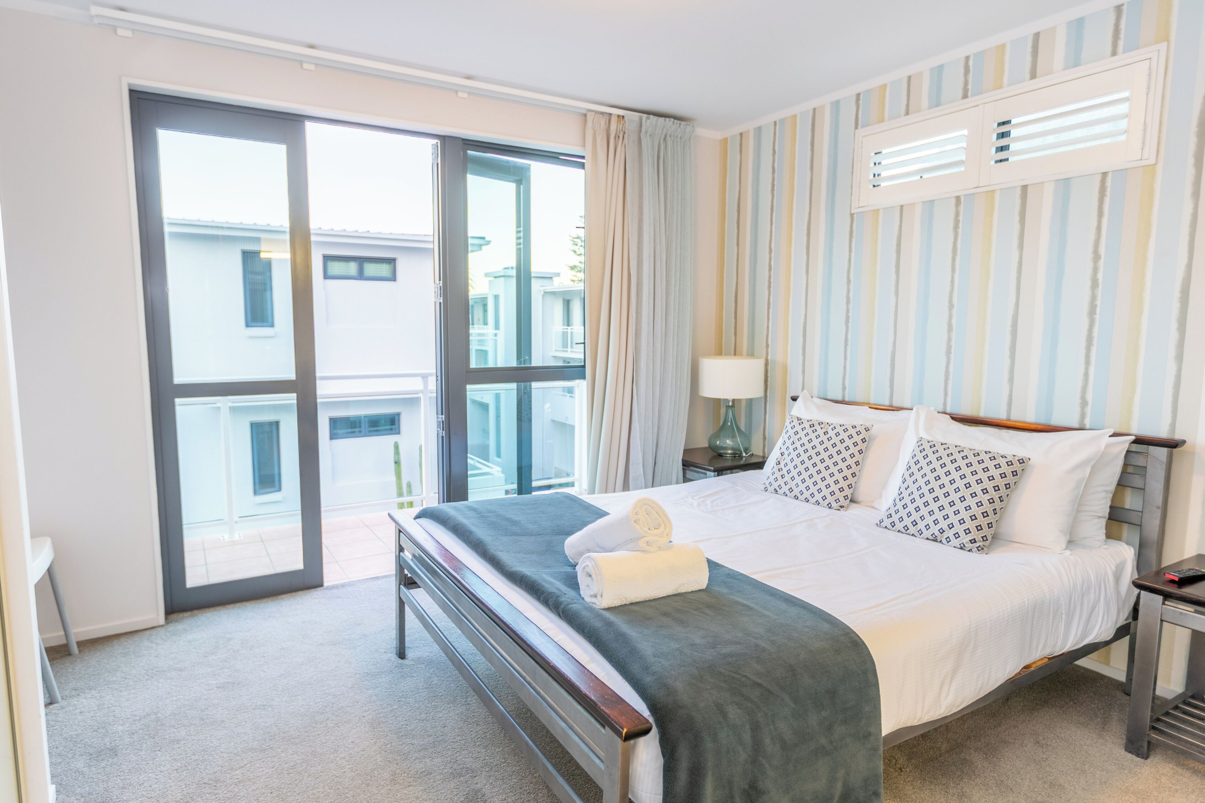 A hotel room with a large bed, a bedside table, a lamp, and a view of the outside through a sliding door.