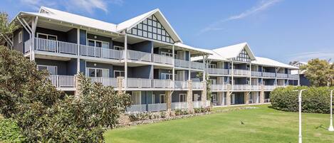 A multi-story hotel with balconies, a lawn, and a clear sky.