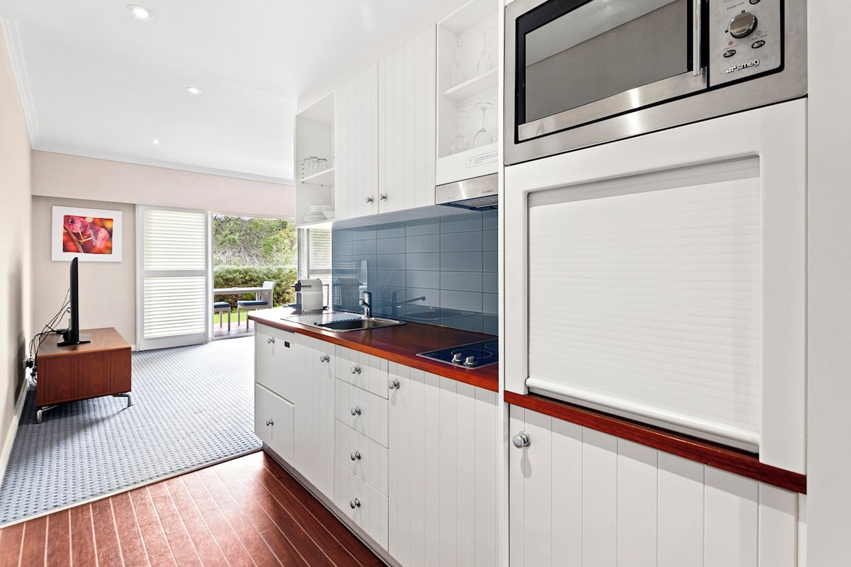 A modern kitchen with white cabinetry, a stainless steel microwave, and a blue tiled backsplash.