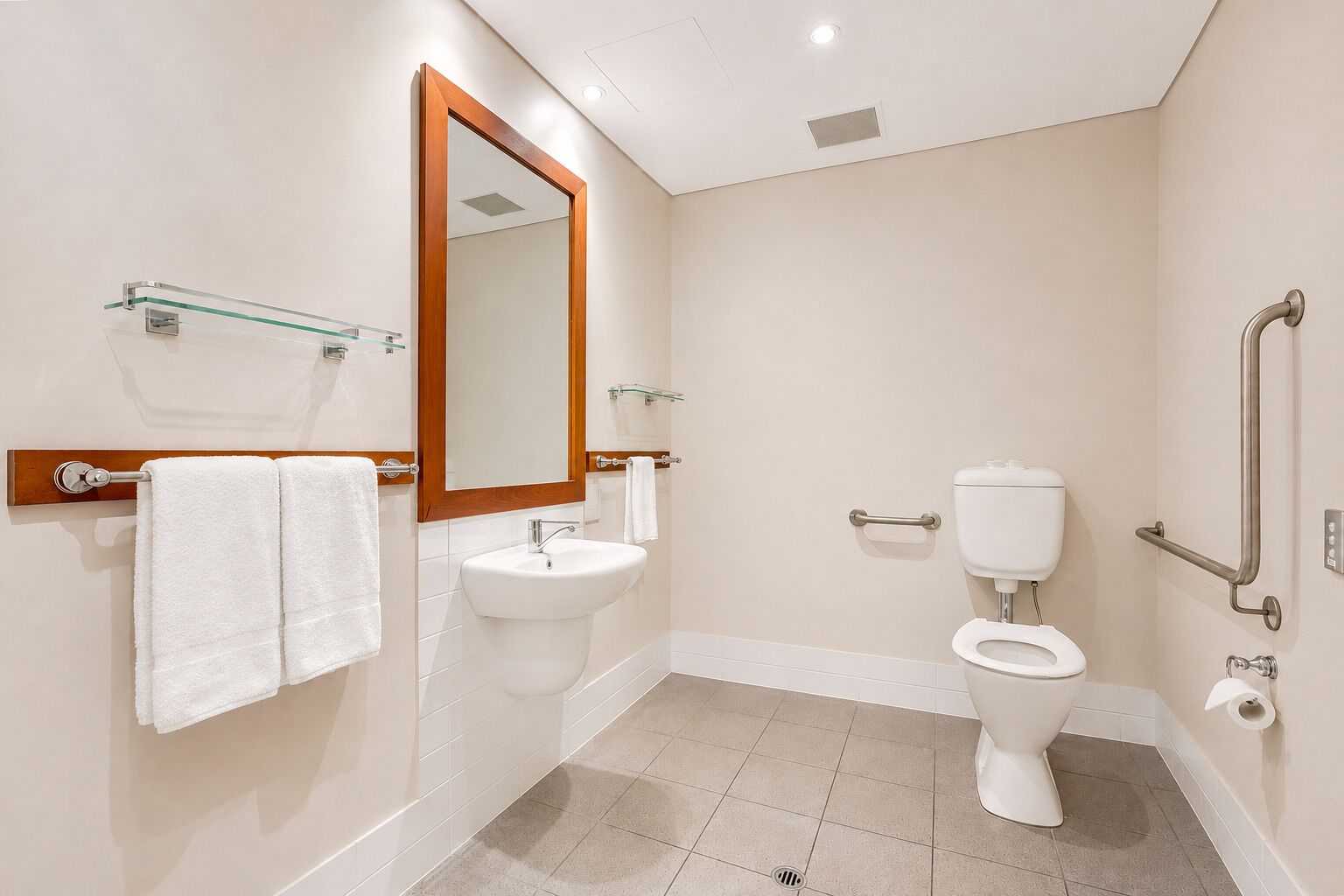 Une salle de bain moderne équipée d’un lavabo, d’un miroir, de toilettes et de barres d’appui.