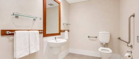 A modern bathroom with a sink, mirror, toilet, and grab bars.