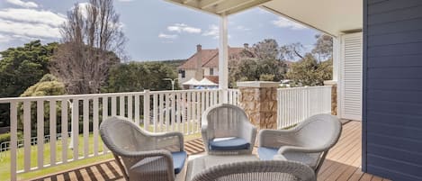 Un espacio de estar al aire libre cubierto con muebles de mimbre y vista a una casa al fondo.
