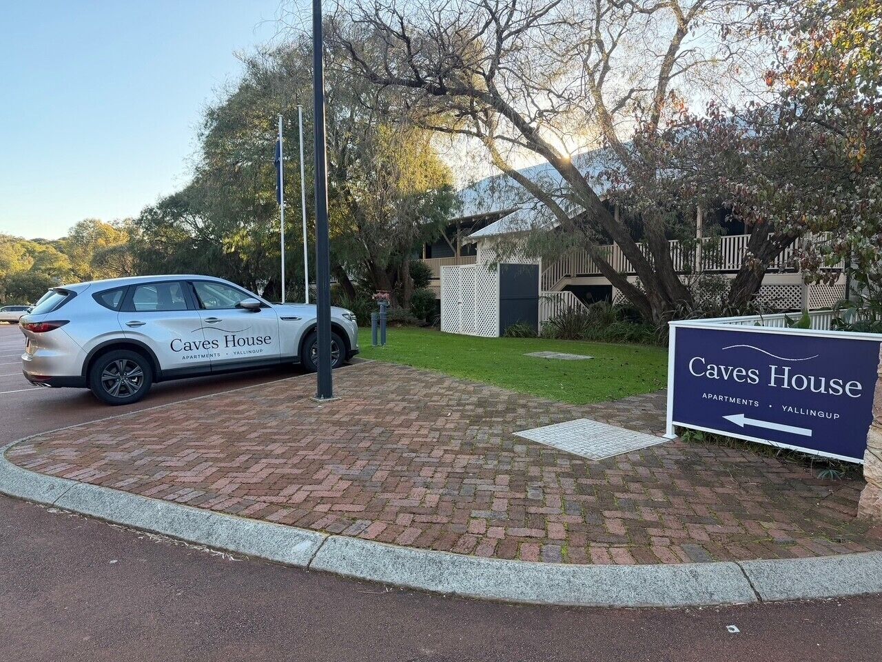 A sign for 'Caves House Apartments' with a paved driveway and a parked car.