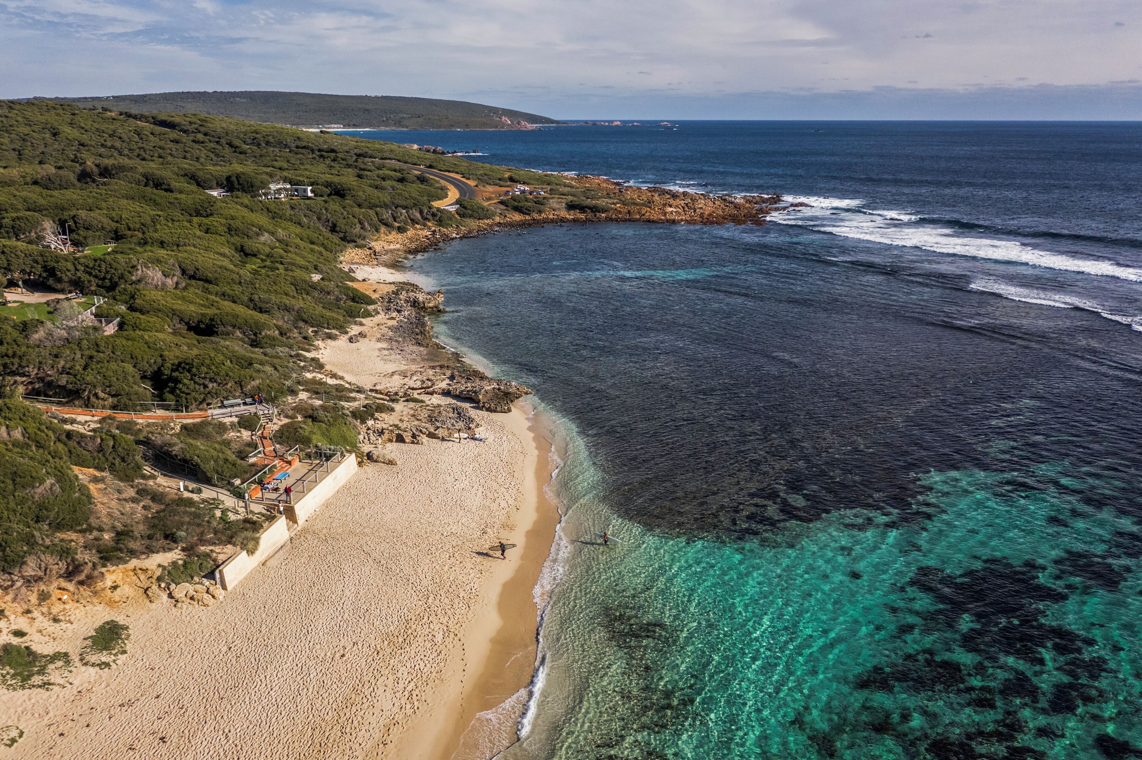 A coastal landscape with a sandy beach, clear turquoise waters, and a rocky shoreline.