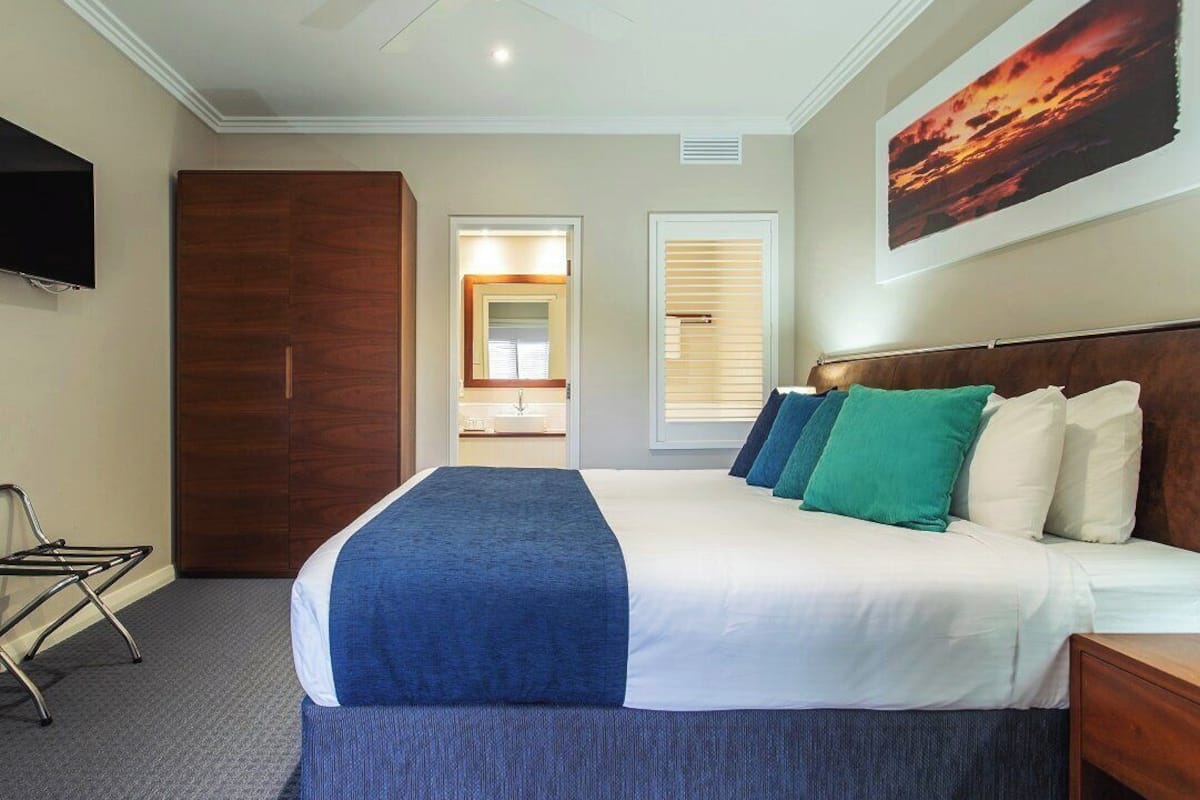 Une chambre d’hôtel avec un lit, une télévision, une armoire en bois, un ventilateur de plafond et un tableau au mur.