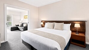 A hotel room with a large bed, a nightstand with a lamp, a sofa, and a view of a balcony. - Caves House Apartments (Yallingup)
