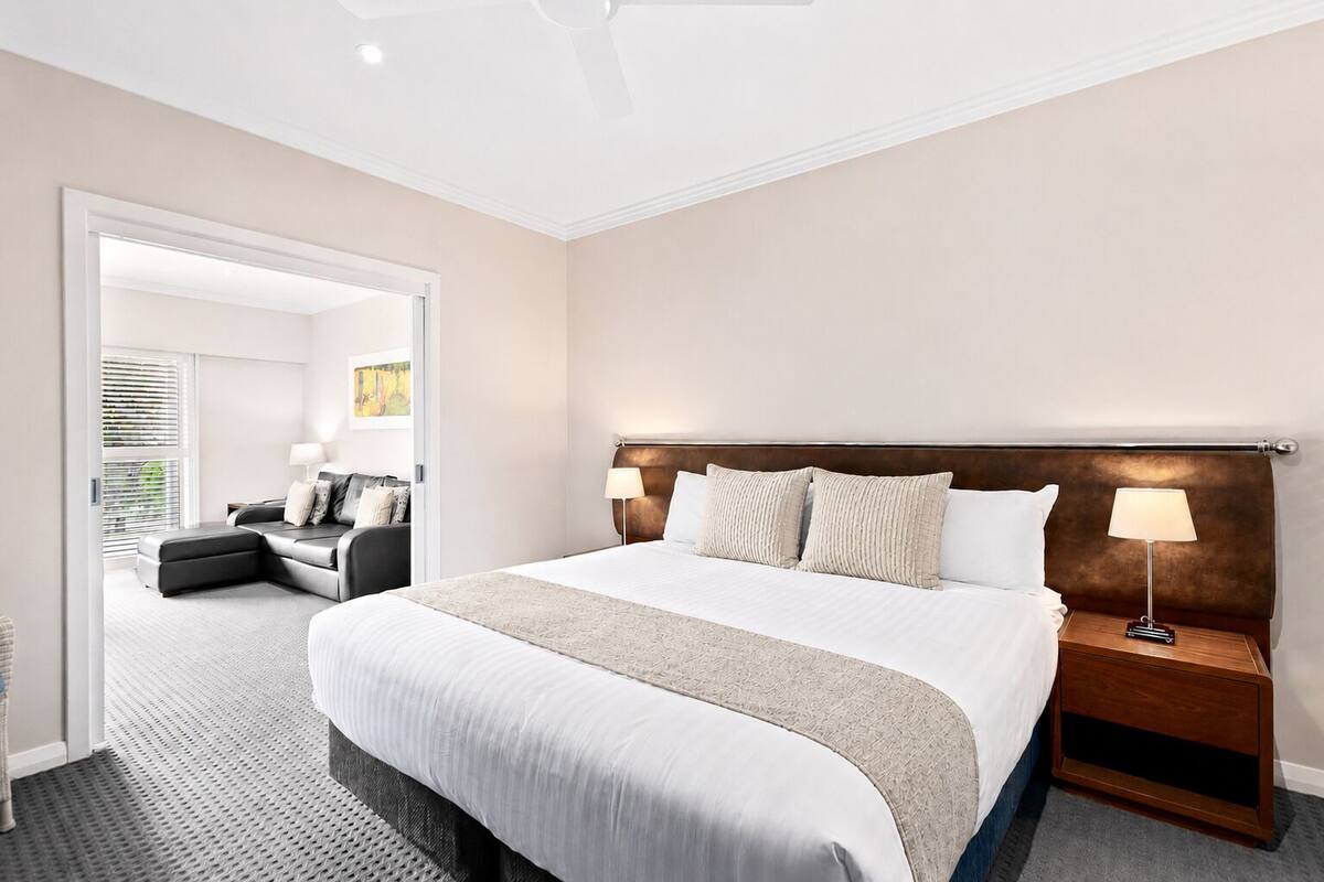 Une chambre d’hôtel avec un grand lit, une table de chevet avec une lampe, un canapé et une vue sur un balcon.