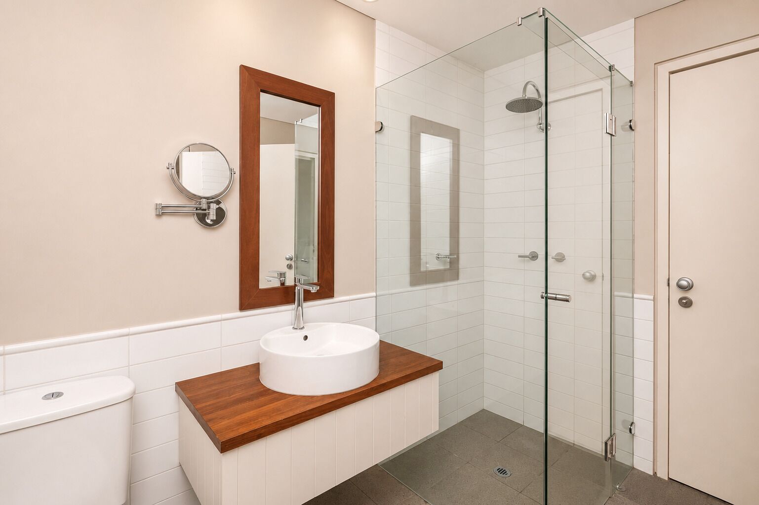 A bathroom with a wooden vanity, a white sink, a mirror, and a glass-enclosed shower.