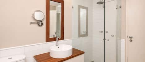 A bathroom with a wooden vanity, a white sink, a mirror, and a glass-enclosed shower.