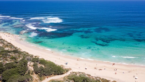 Vista aerea di una spiaggia con acque cristalline turchesi, spiaggia sabbiosa e vegetazione rada.