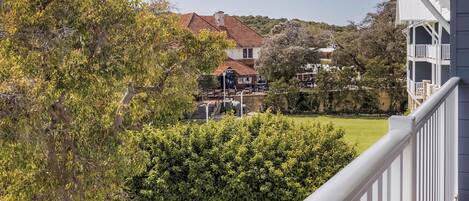 Un balcón con vistas a un jardín ajardinado, un árbol y un edificio distante.