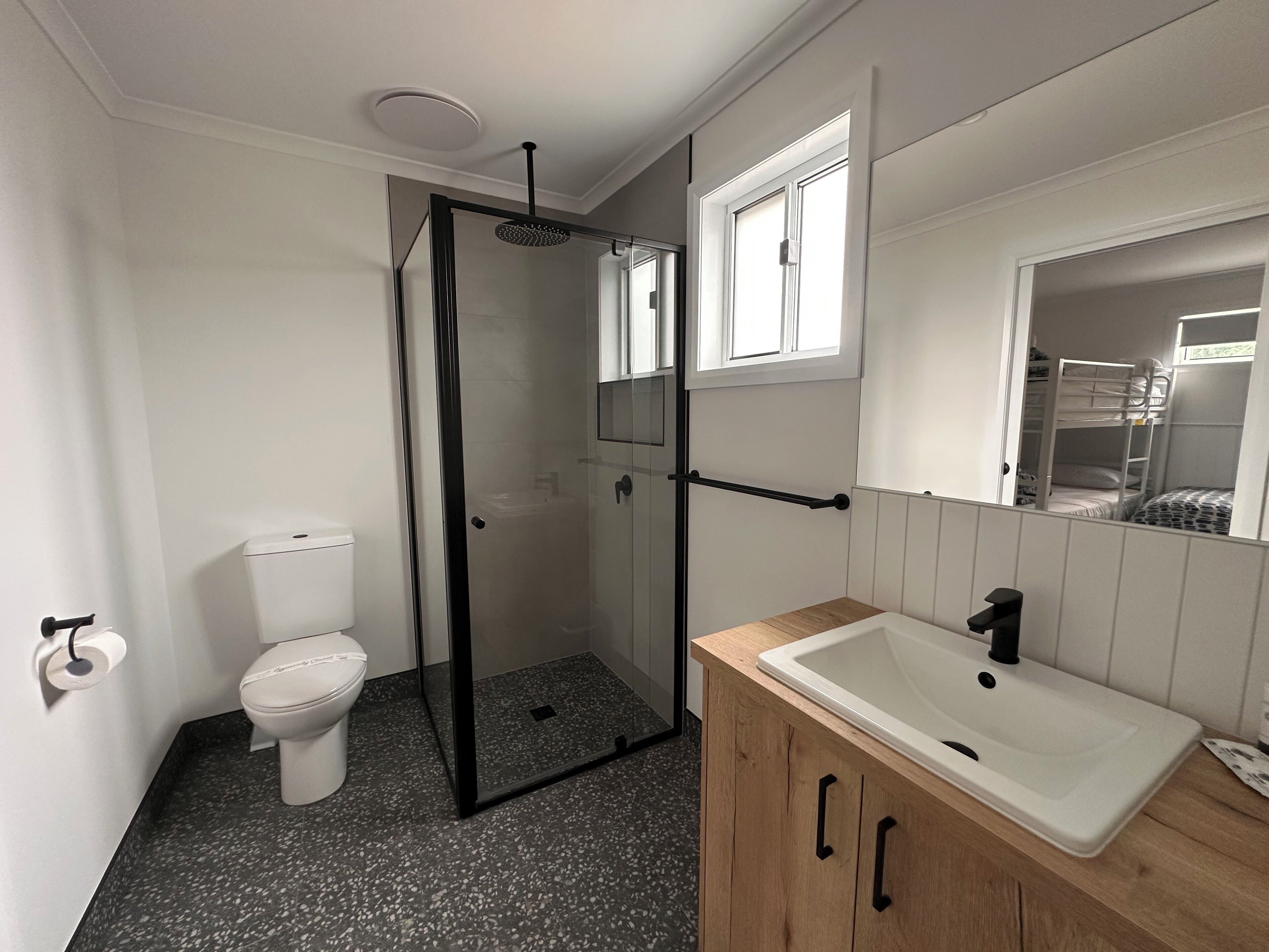 Une salle de bain comprenant des toilettes, une douche à parois de verre, un meuble-lavabo en bois et un miroir.