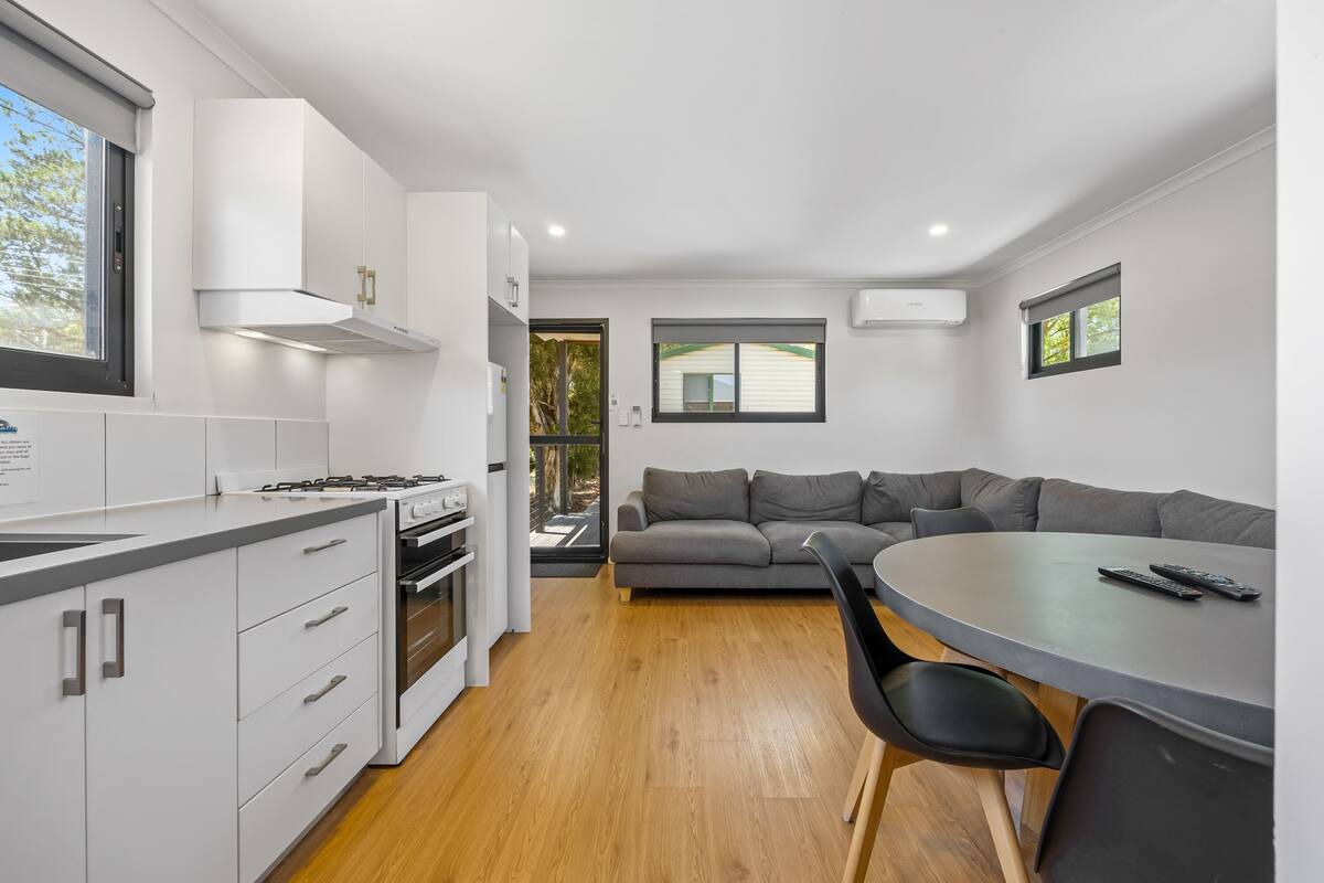 A modern kitchen with white cabinets, a stove, and a dining area with a gray table and black chairs.