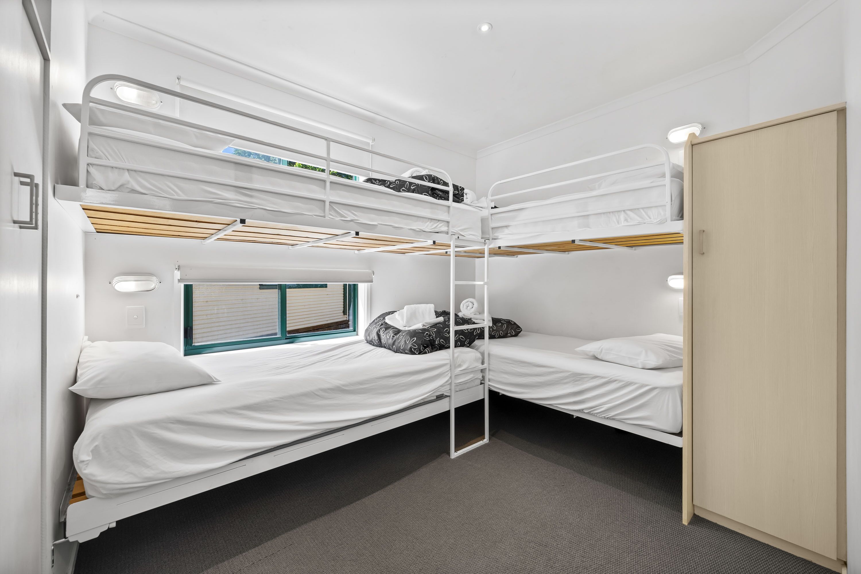 Une chambre avec deux lits superposés, une fenêtre avec des stores et une porte.