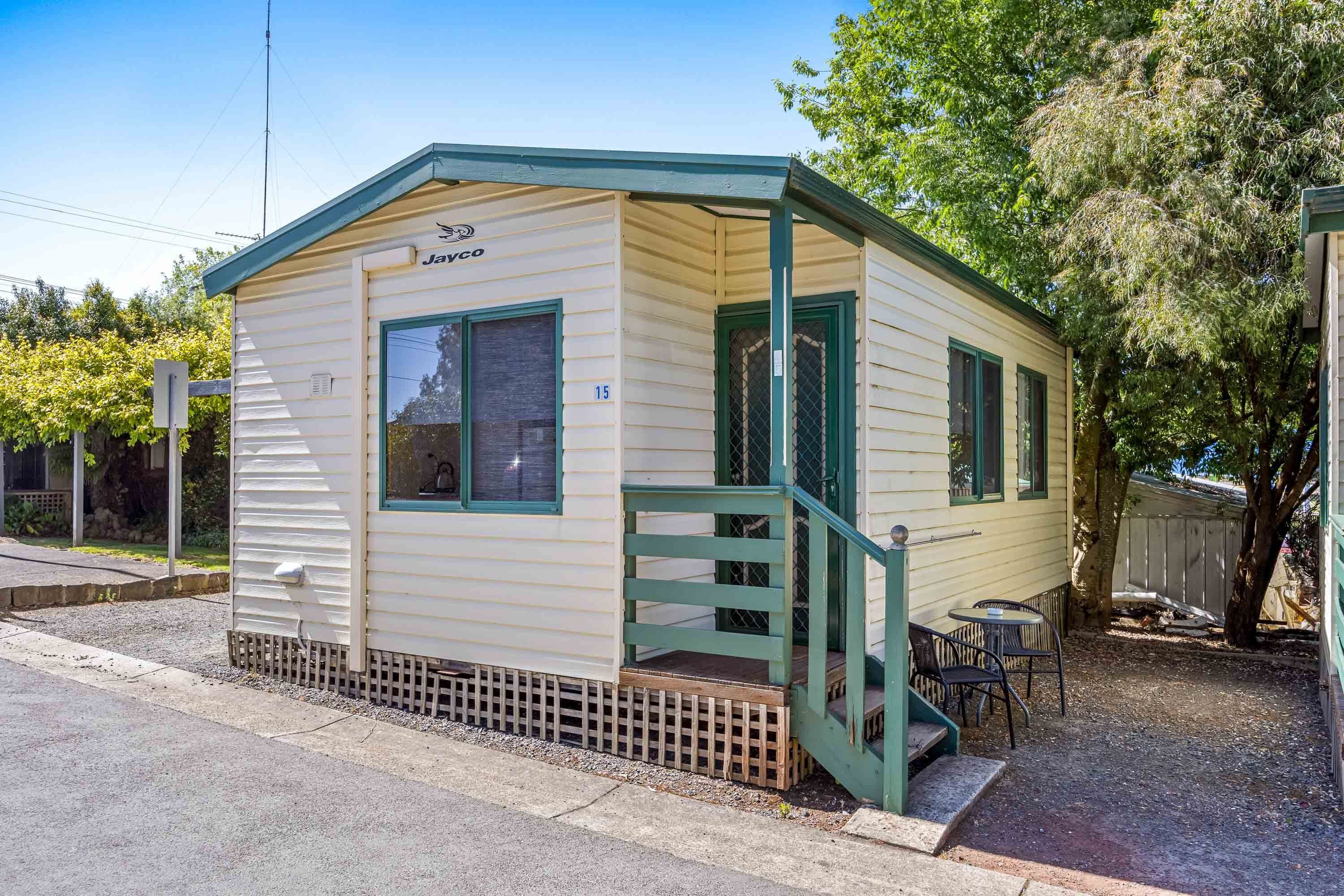 A small, single-story mobile home with a green porch and a small table and chairs outside.