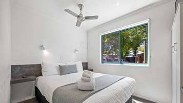 A modern bedroom with a bed, bedside tables, a ceiling fan, and a window with a view of the outside.