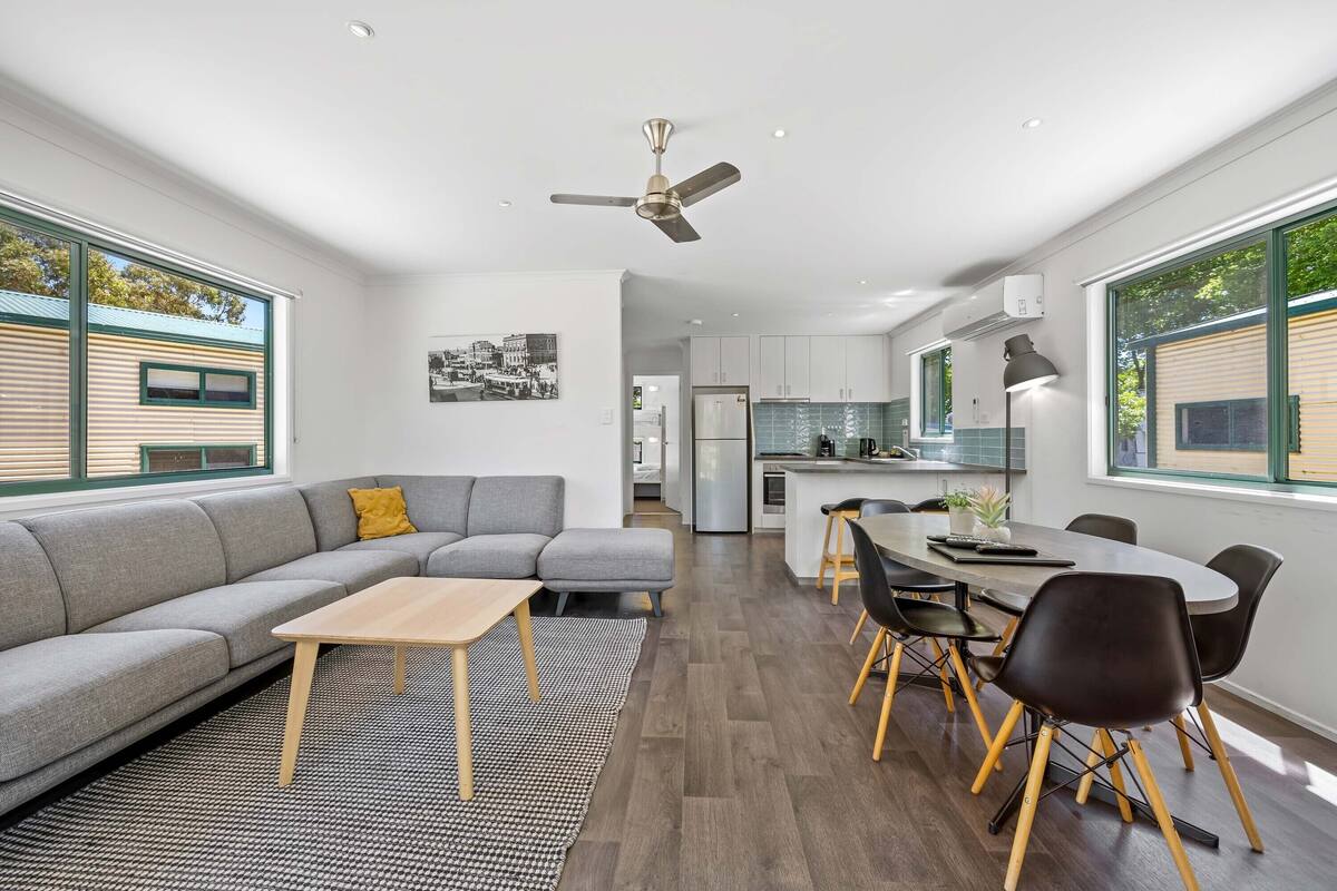 A modern living room with a gray sectional sofa, a wooden coffee table, and a dining area with a round table and chairs.