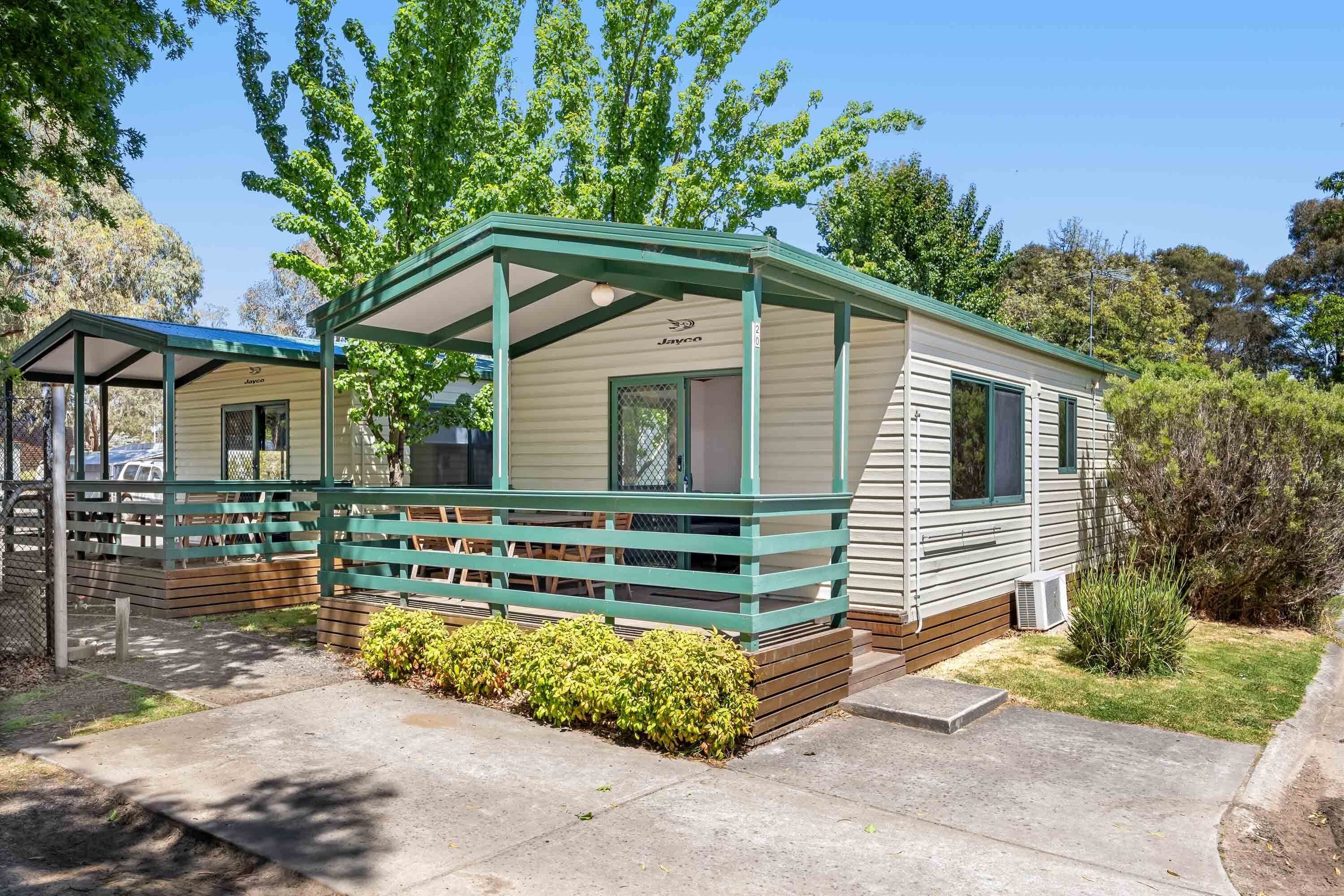 A mobile home with a covered porch, a small garden, and a clear sky.