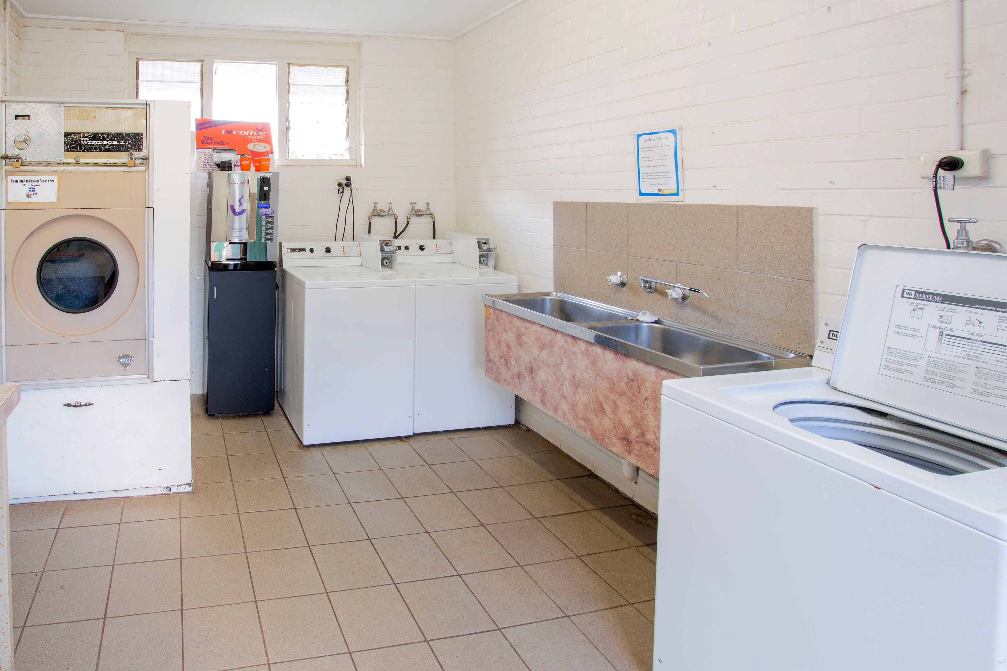 A laundry room with a front-loading washer, a dryer, a sink, and a coffee machine.