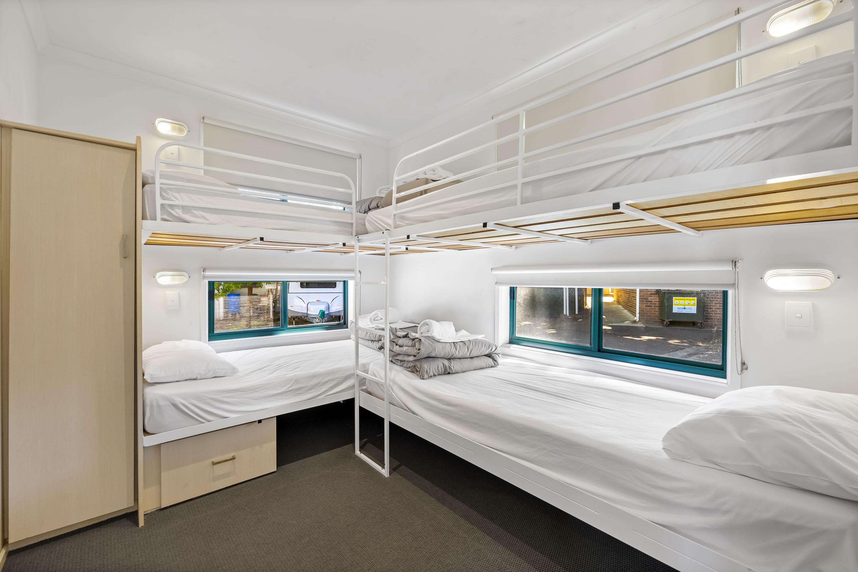 A compact, well-lit room with bunk beds, a window with a view of the outside, and a small storage cabinet.