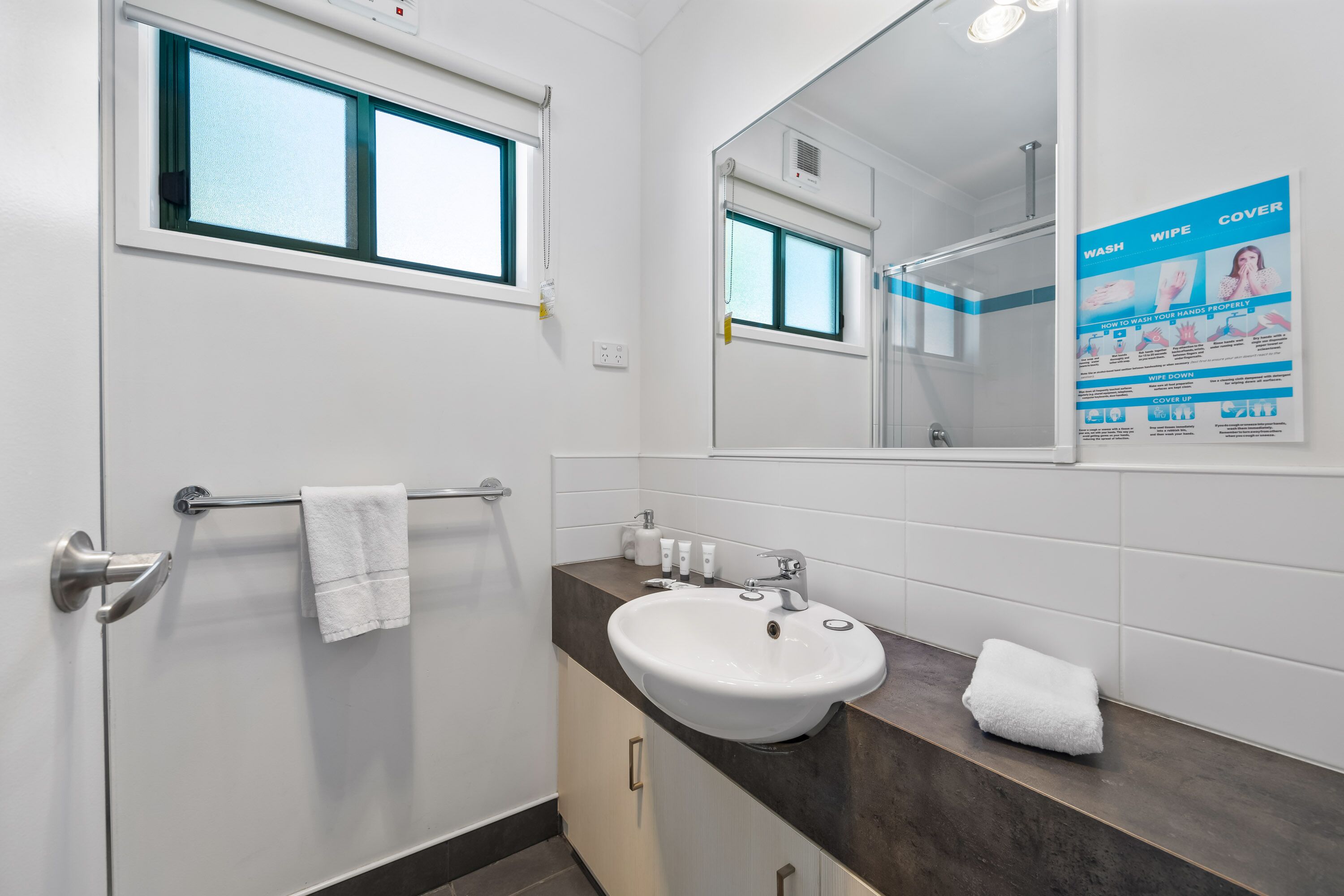 A modern bathroom with a white sink, a towel rack, a mirror, and a window.