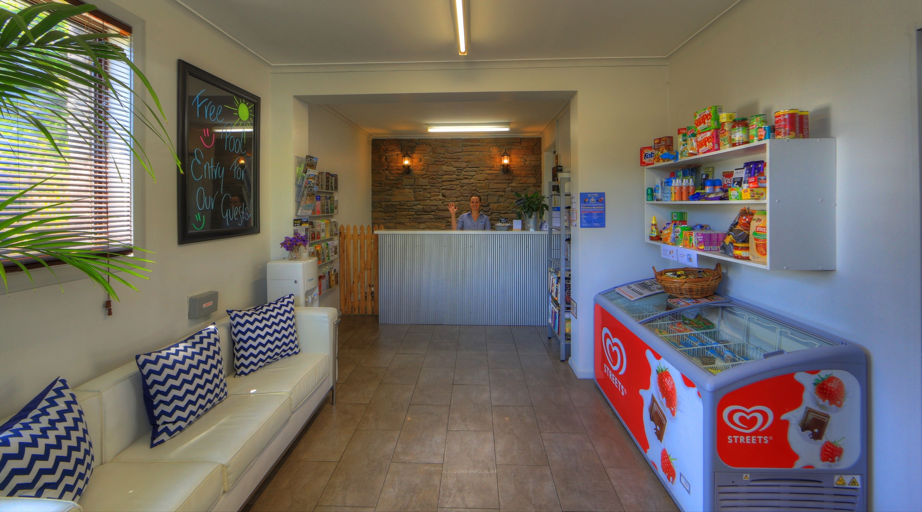 A reception area with a counter, a white sofa with patterned cushions, a stone wall, and a freezer stocked with food items.