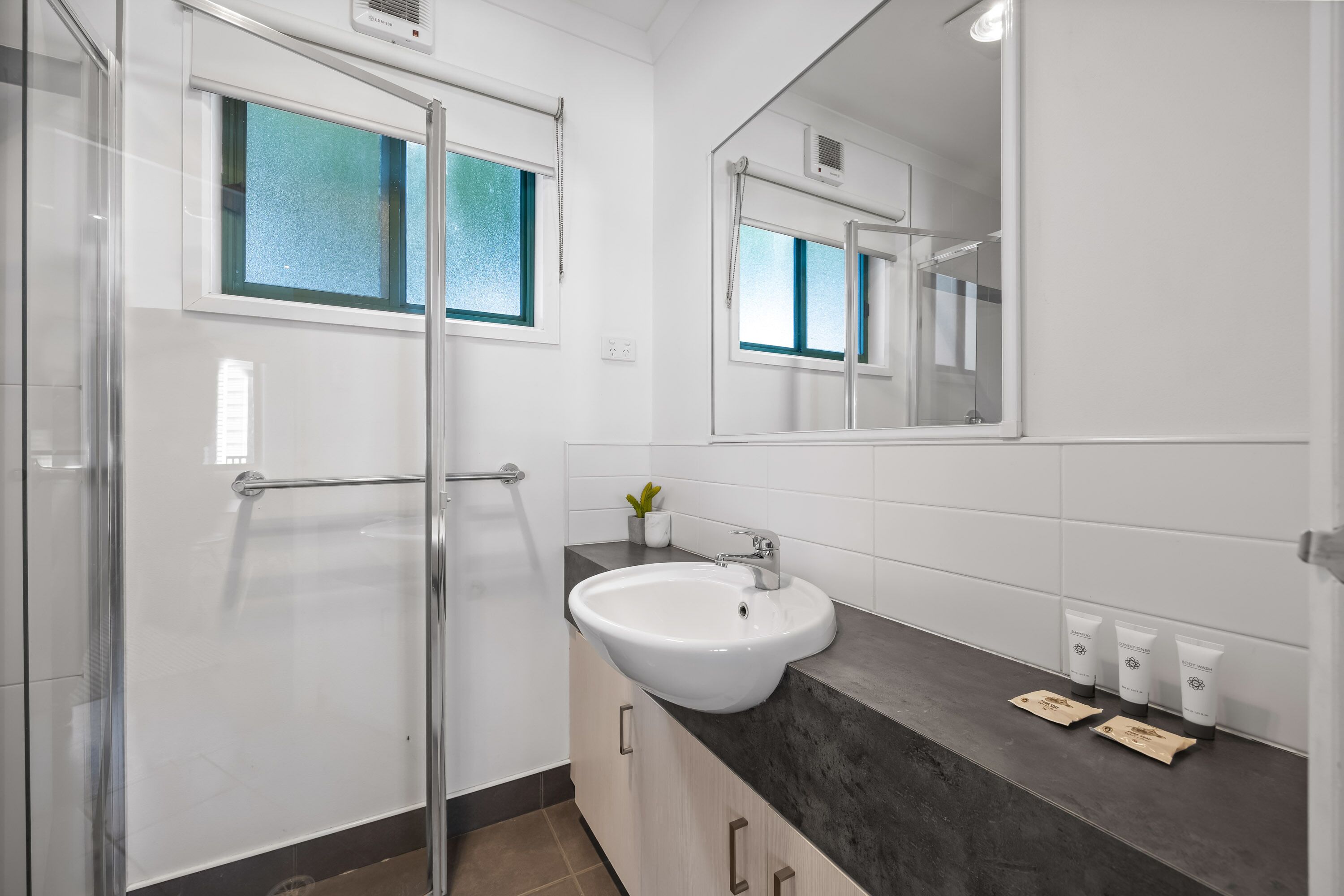 A modern bathroom with a glass shower enclosure, a white sink, and a large mirror.