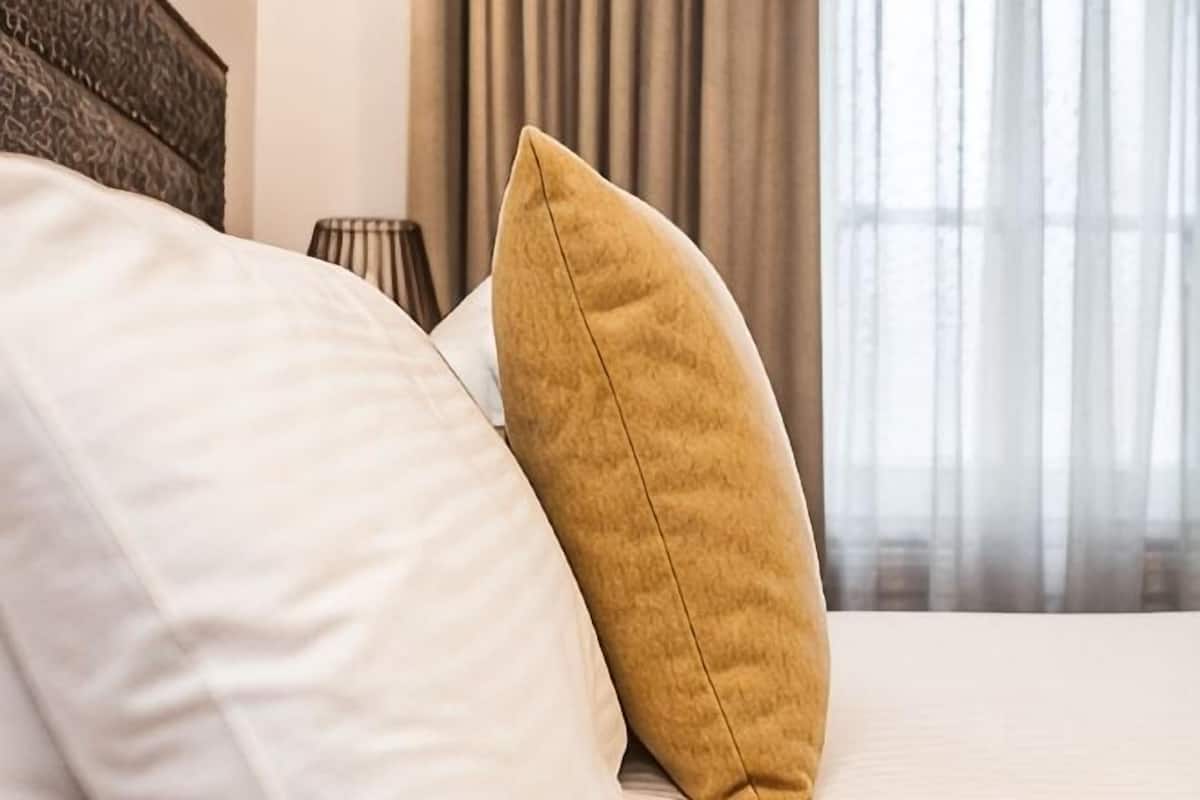 A bed with white and mustard pillows, a lamp, and a window with curtains.