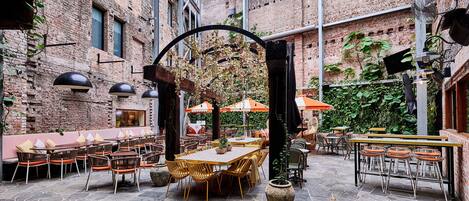 An outdoor patio with brick walls, stone flooring, and various seating arrangements including tables and chairs.