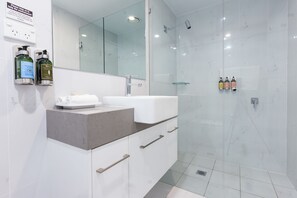 Features a sleek vanity, marble countertop, and large mirror, along with a glass-enclosed shower and handheld showerhead.