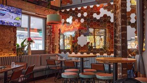 A cozy restaurant with brick walls, hexagonal mirrors, and a neon sign. Tables and chairs are arranged for dining. - The Lucky Hotel (Newcastle)