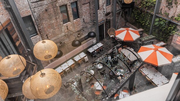 An outdoor dining area with wicker pendant lights, tables, and orange and white striped umbrellas. - The Lucky Hotel (Newcastle)