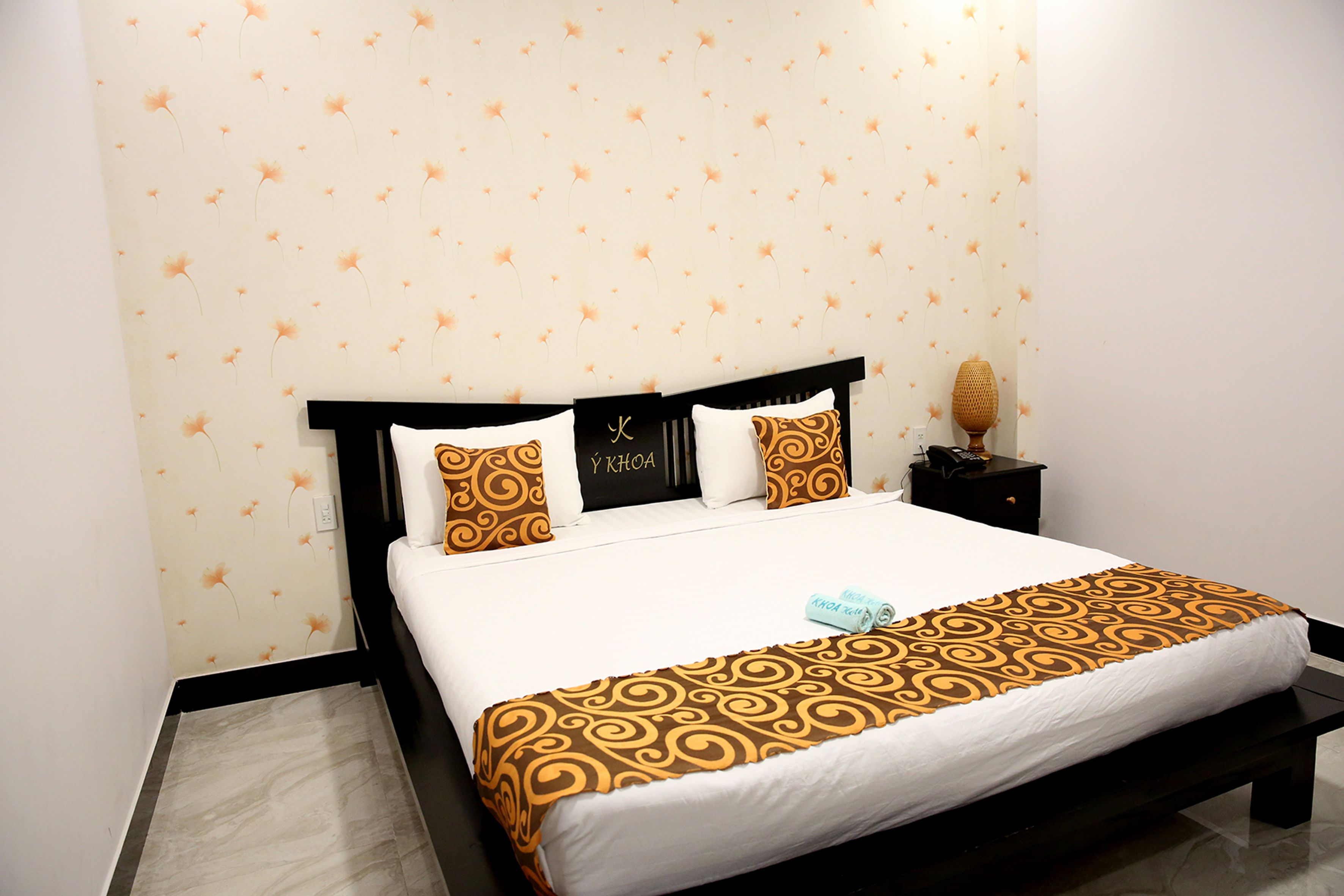 Una cama bien hecha con una colcha estampada, una lámpara de noche y un reloj de pared.