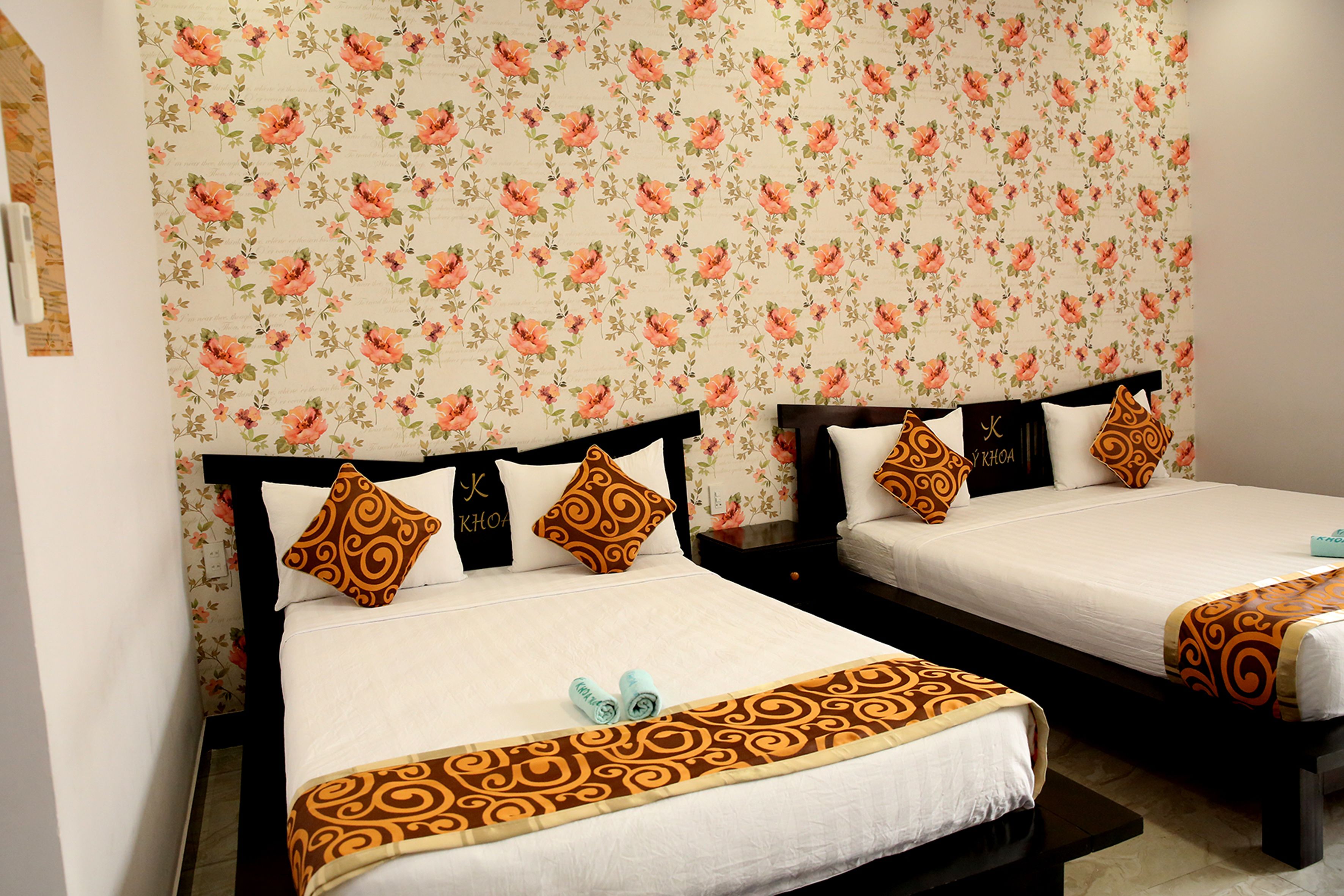 A hotel room with two beds, floral wallpaper, and a black headboard.