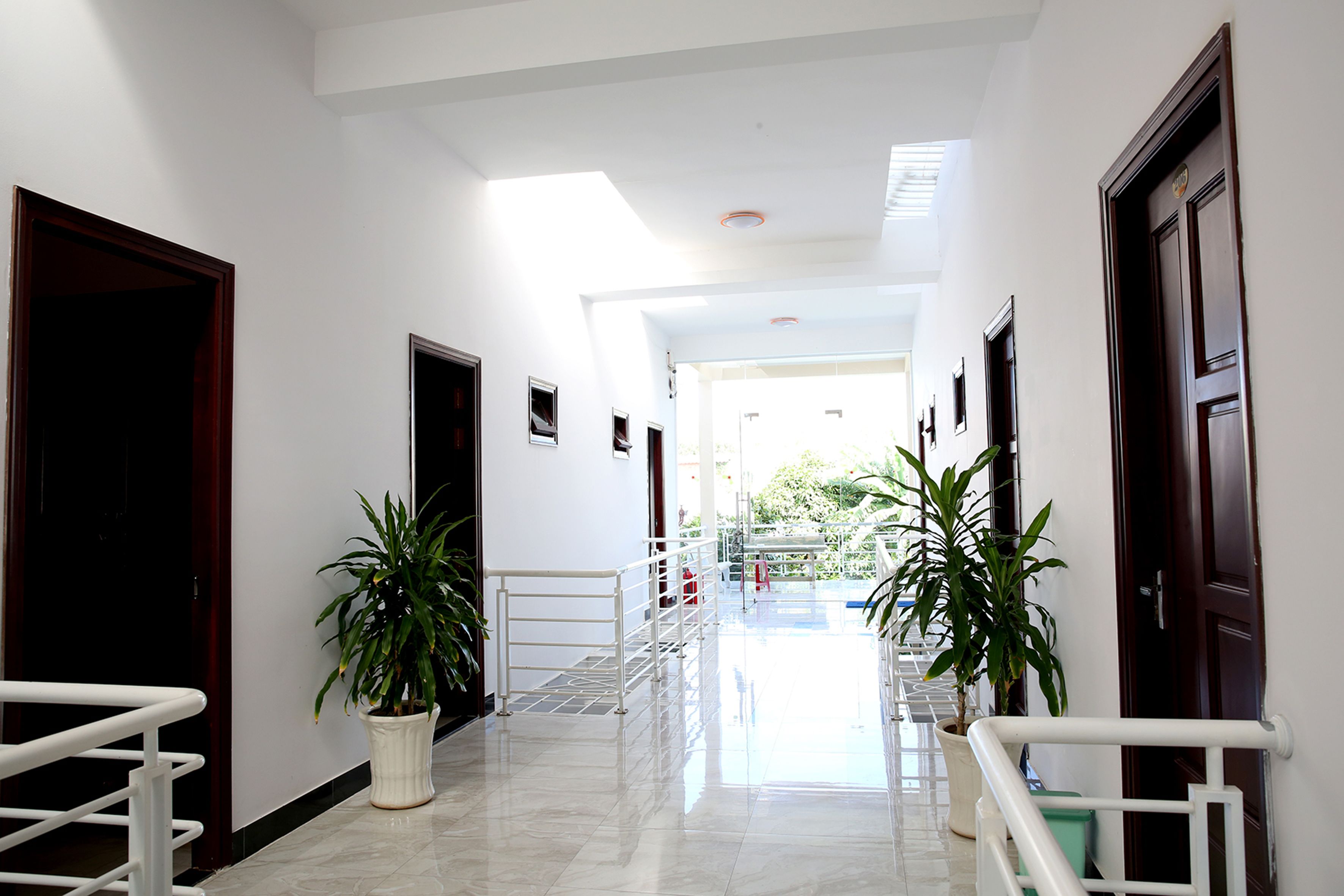 A hotel hallway with white walls, a tiled floor, and potted plants.
