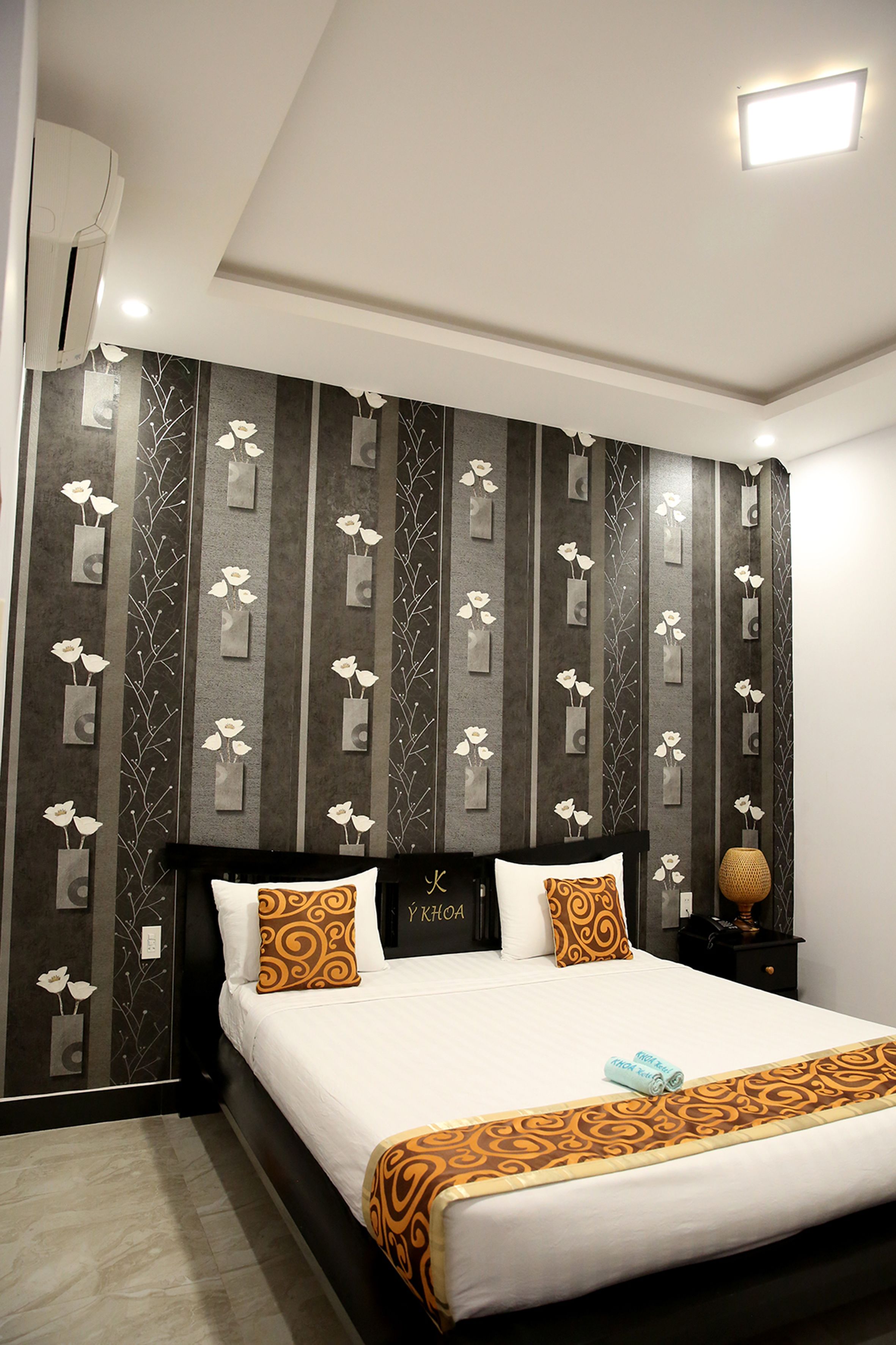 Habitación de hotel con una cama, cabecero, mesita de noche y una pared con estampado floral.