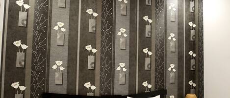 Habitación de hotel con una cama, cabecero, mesita de noche y una pared con estampado floral.