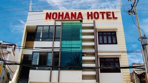 Un hotel llamado "NOHANA HOTEL" con fachada moderna, ventanas grandes y una puerta de garaje amarilla.
