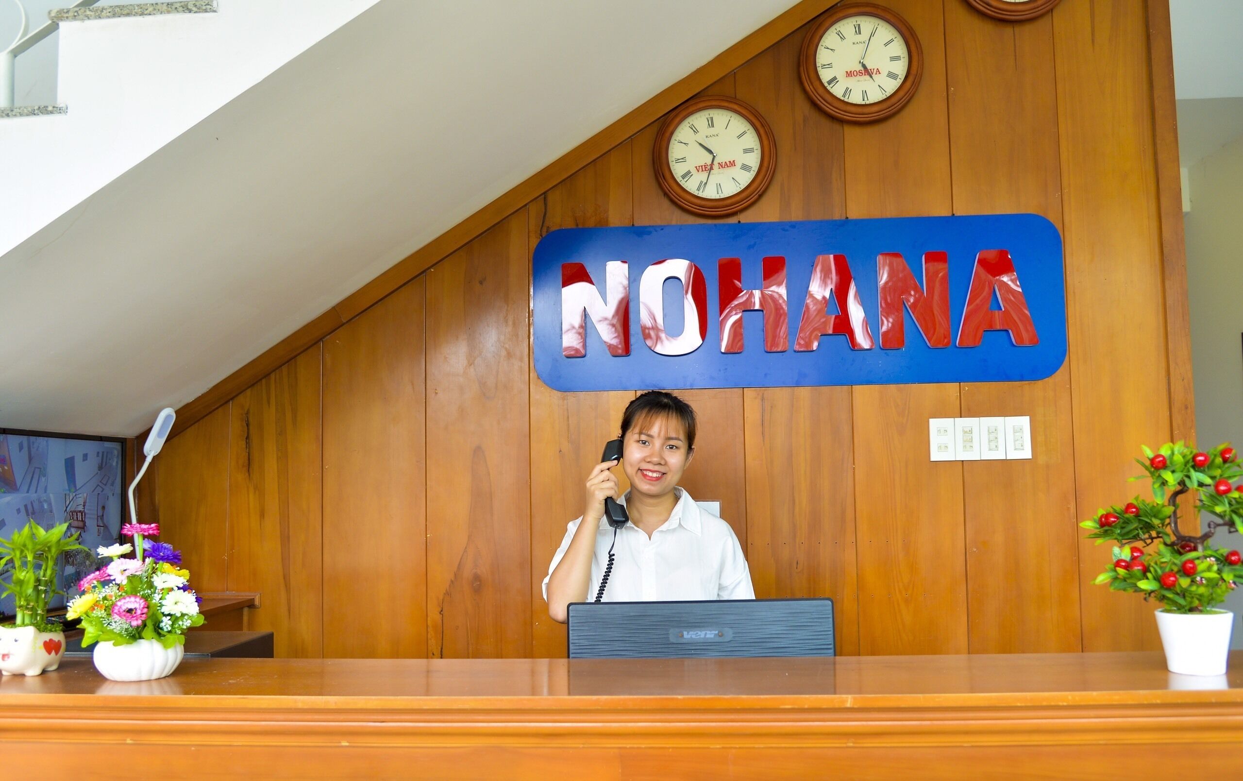 A reception desk with a wooden backdrop, a clock, and a sign that reads "NOHANA".