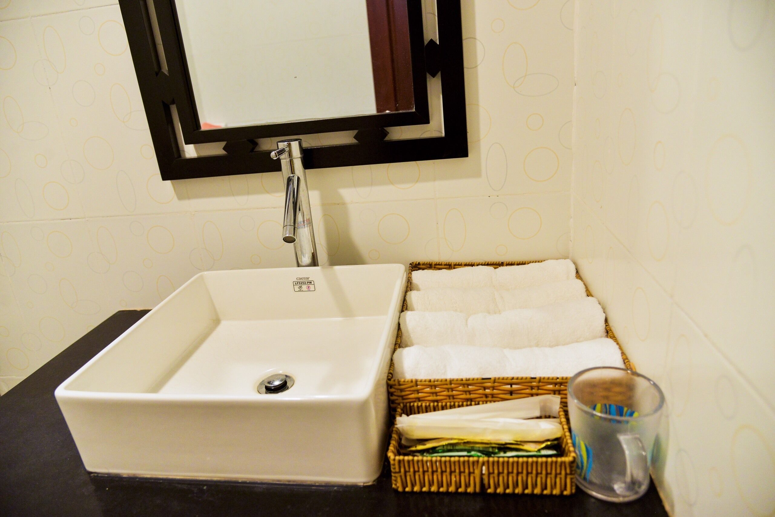 A bathroom sink with a mirror, a wicker basket with folded towels, and a glass of water.