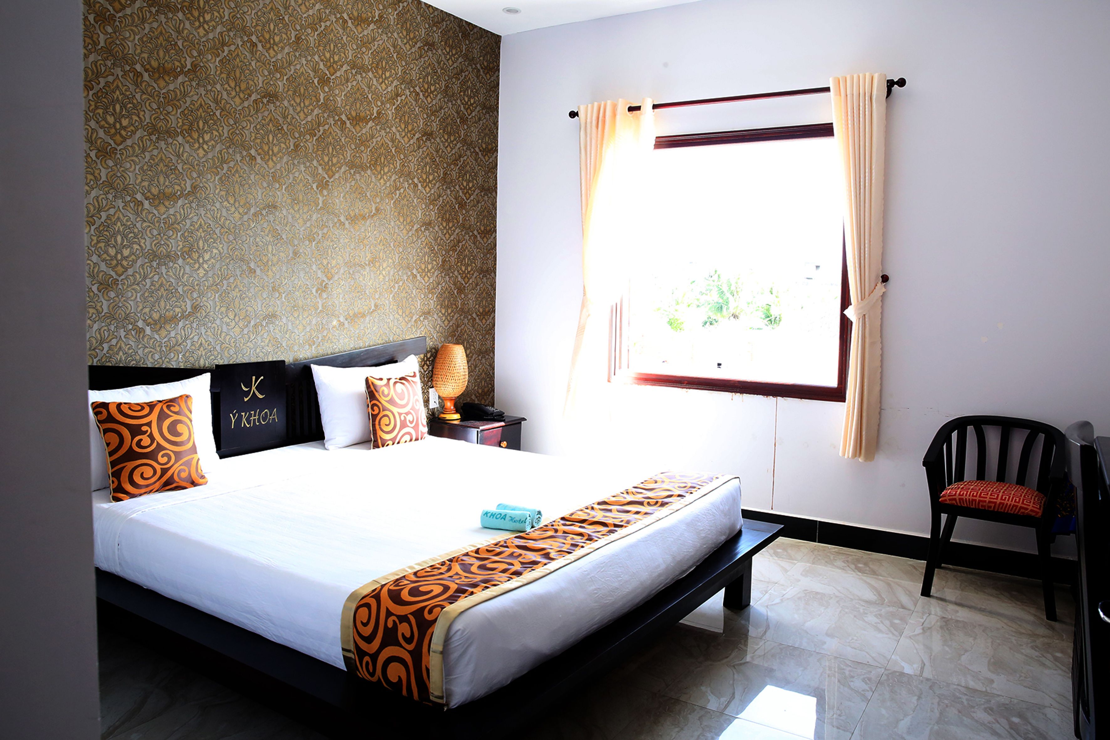 A hotel room with a large bed, a nightstand, a chair, and a window with curtains.