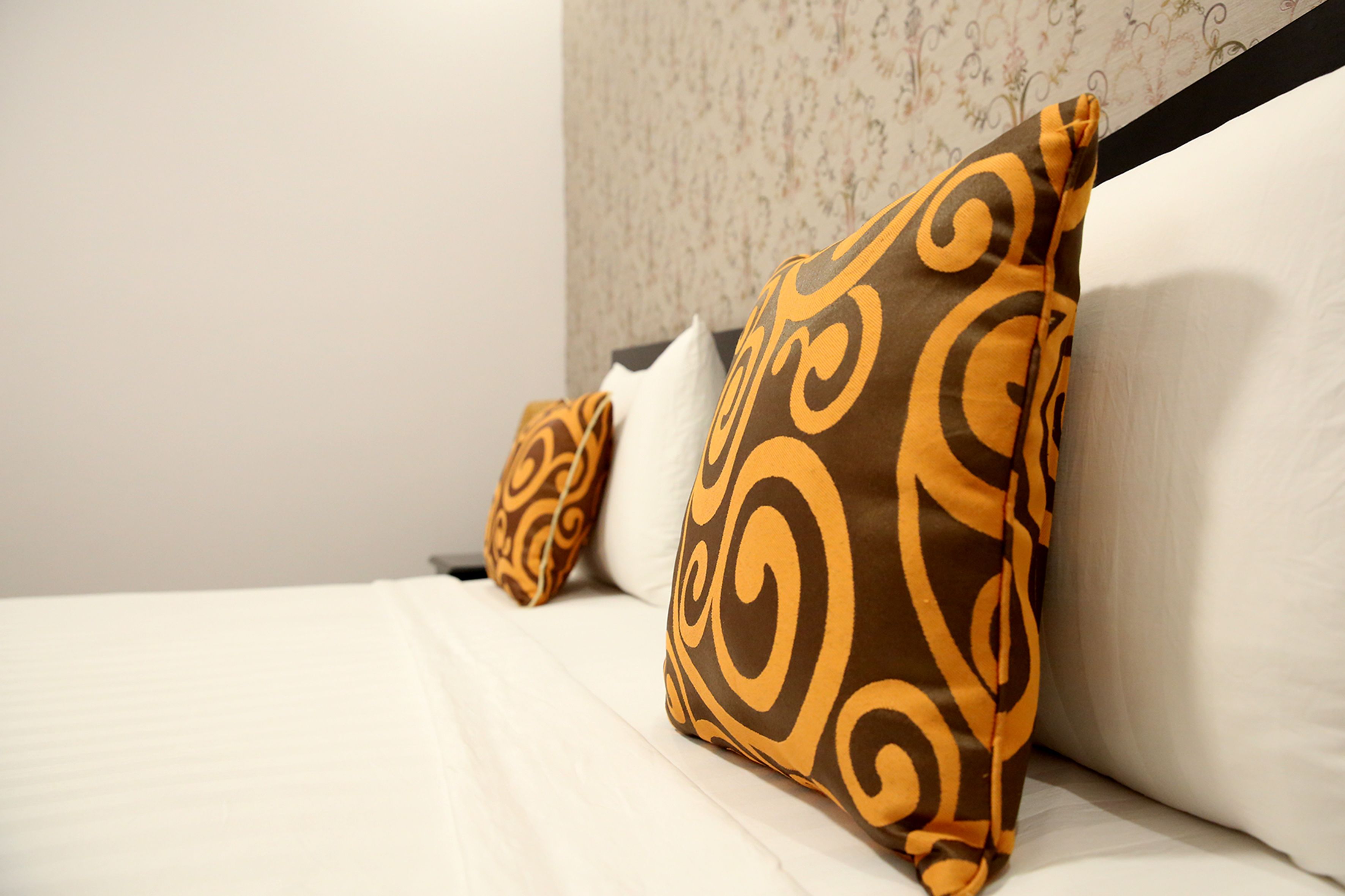 A bed with white bedding and two decorative pillows with a swirl pattern.