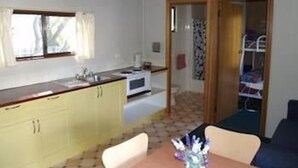 A compact kitchen with a window, a sink, and a microwave. There is a dining area with a table and chairs, and a bunk bed in the background. - Launceston Holiday Park Legana (Legana)