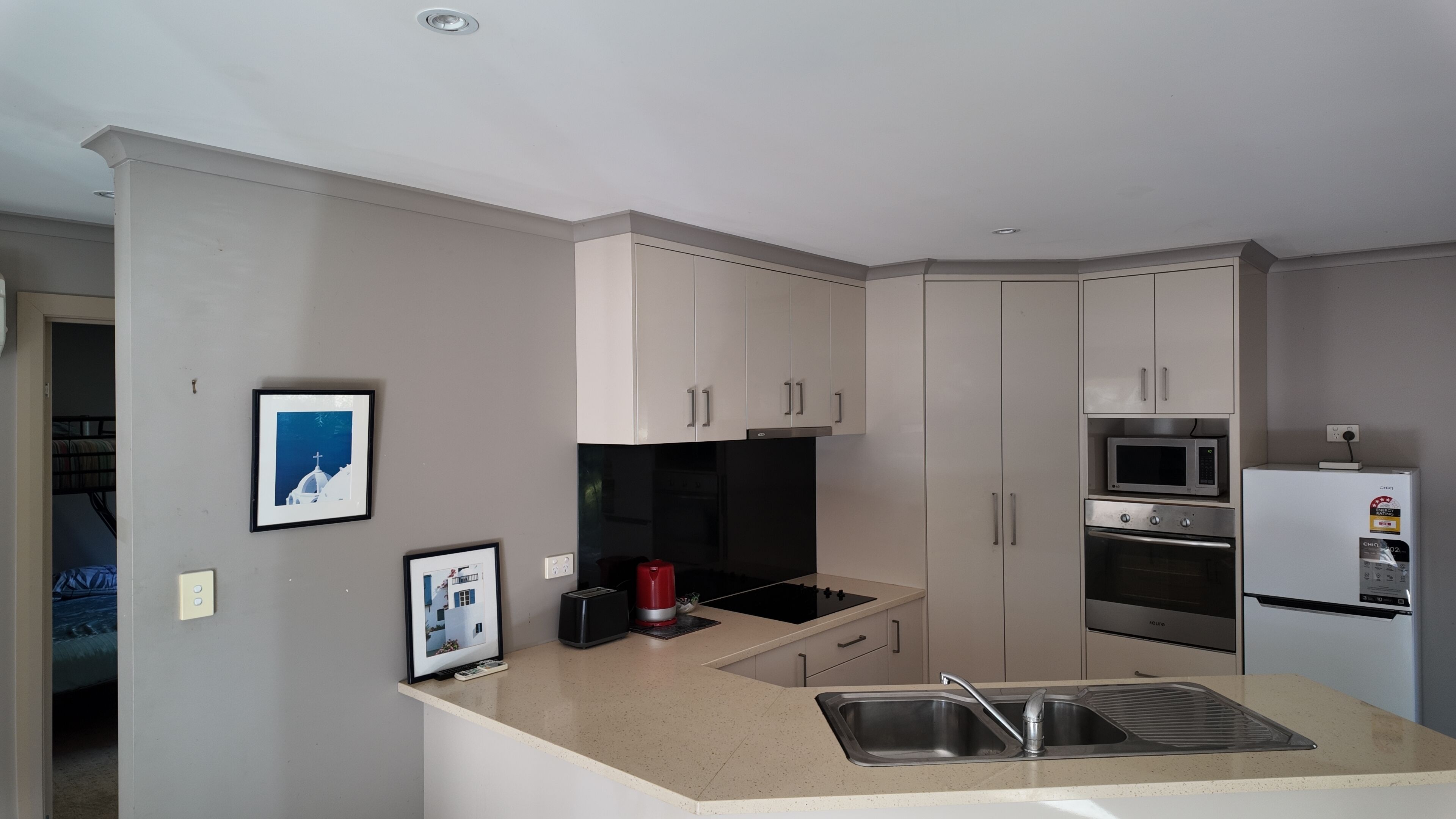 A compact kitchen with a microwave, oven, and a small refrigerator. There is a sink with a modern faucet, and the kitchen has a neutral color scheme.