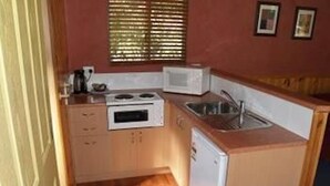 A compact kitchen with a stove, microwave, sink, and small refrigerator. - Launceston Holiday Park Legana (Legana)